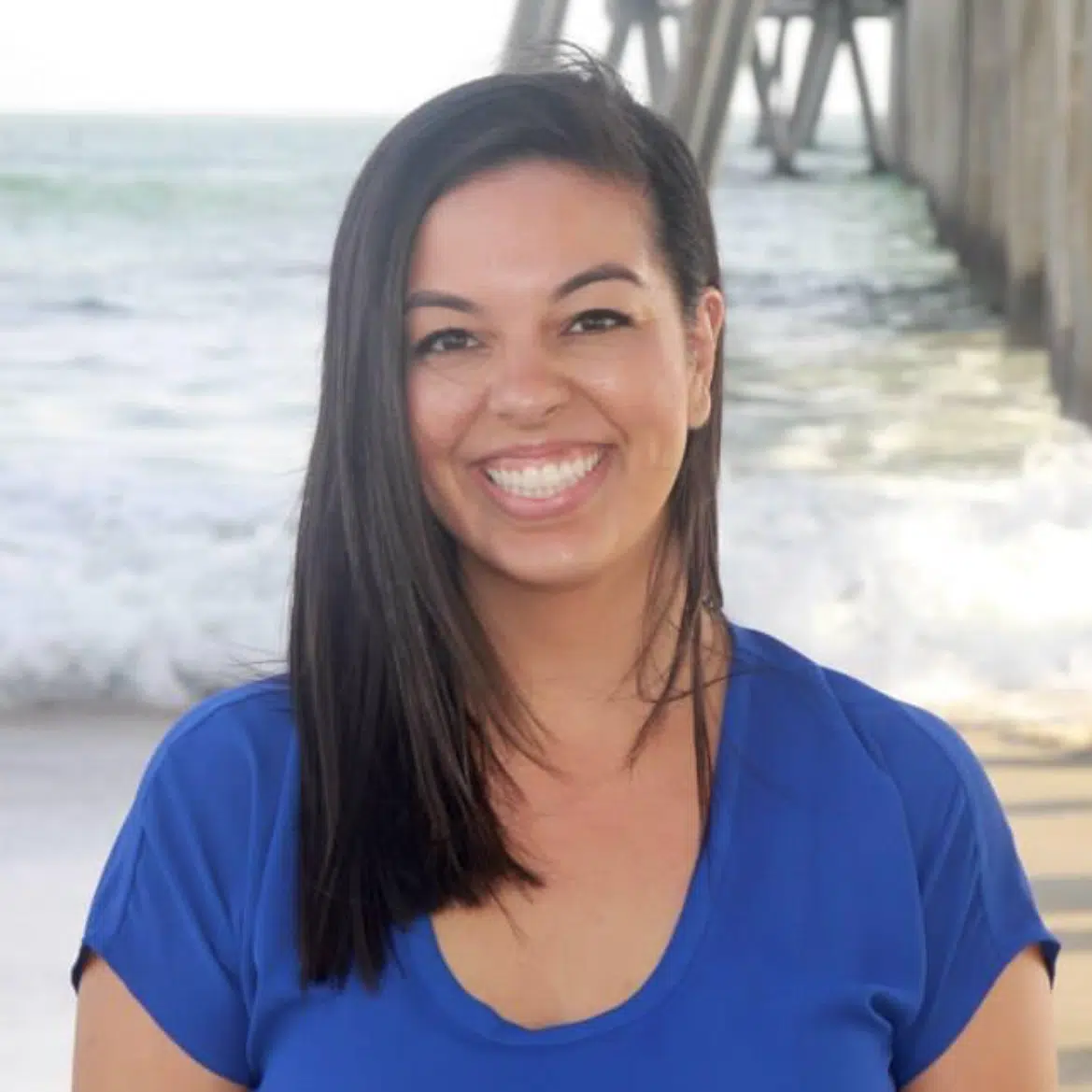 A woman smiling in front of a pier.