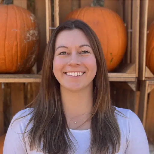 A woman smiling in front of pumpkins.
