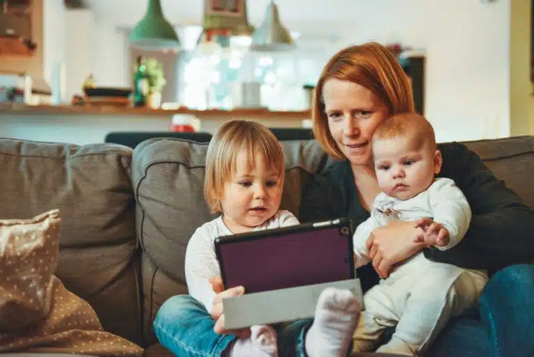 A woman with two small children sitting on a couch with a tablet.