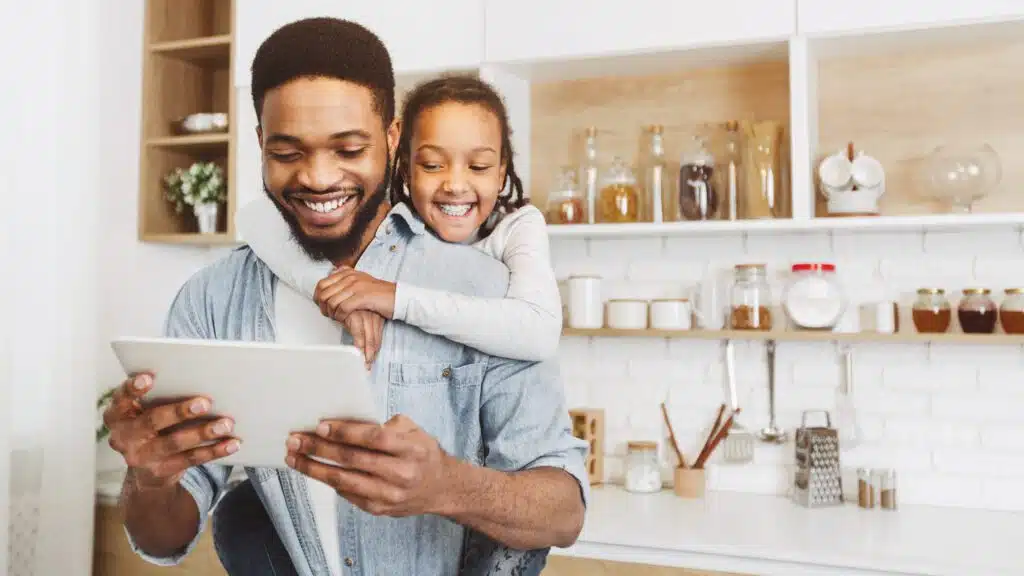 An african-american man and his daughter using a tablet computer in the kitchen.