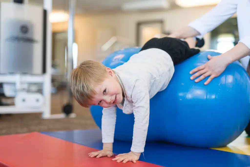 A young boy is playing with an exercise ball in a gym.