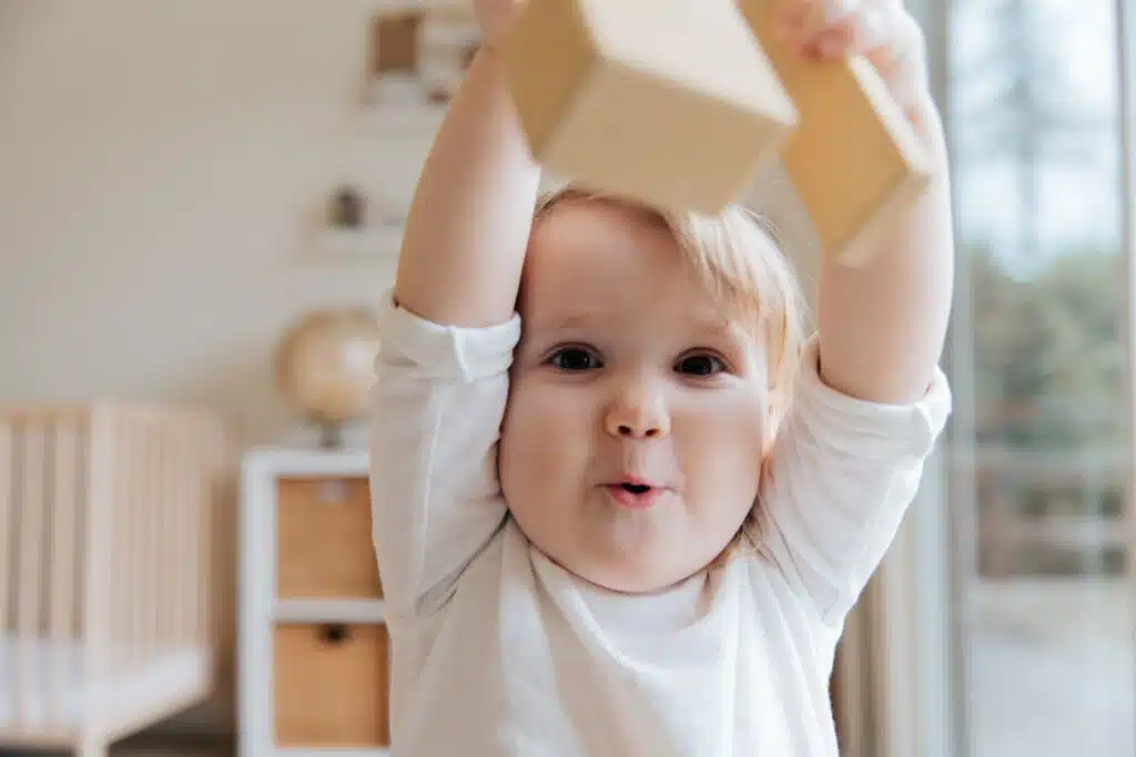 A baby is playing with a wooden block in a room.