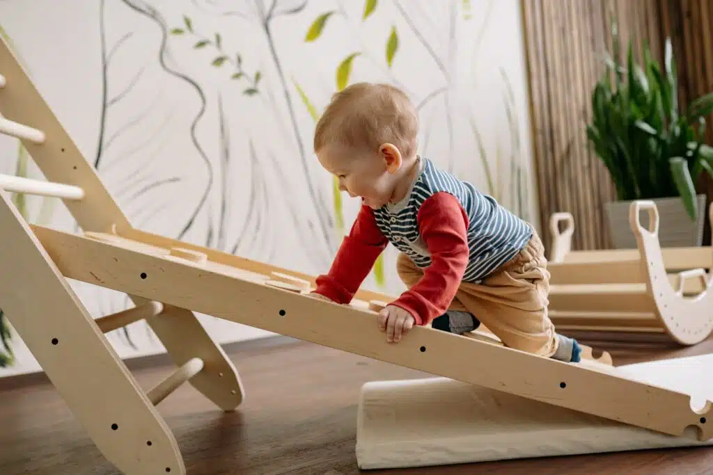 A baby is playing with a wooden slide in a room.